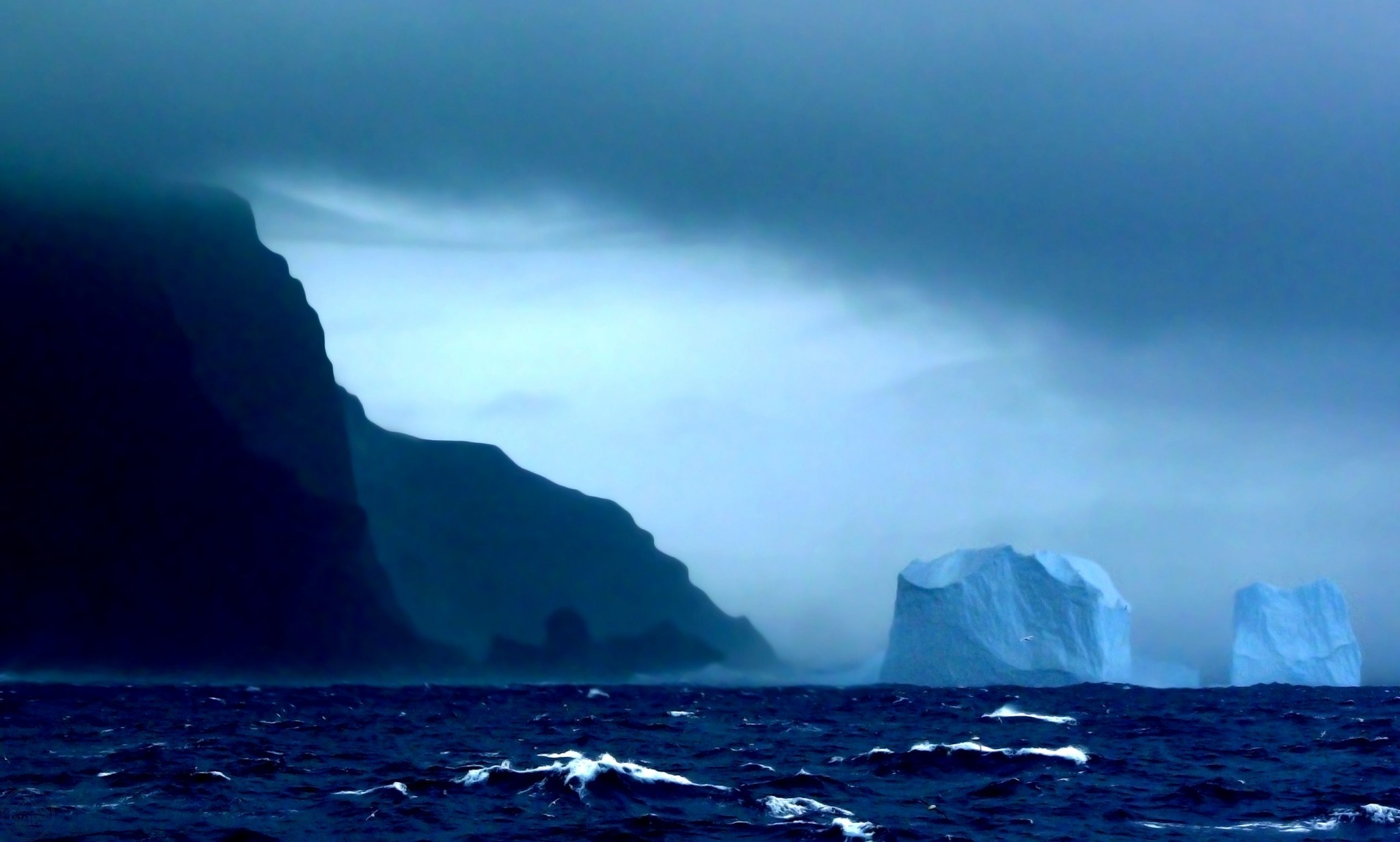 Falaises sombres de l’île Bouvet et deux icebergs sous un ciel chargé